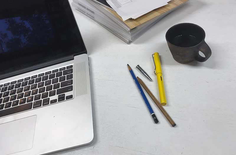 マックのノートパソコンと万年筆。鉛筆と陶製のコーヒーカップ